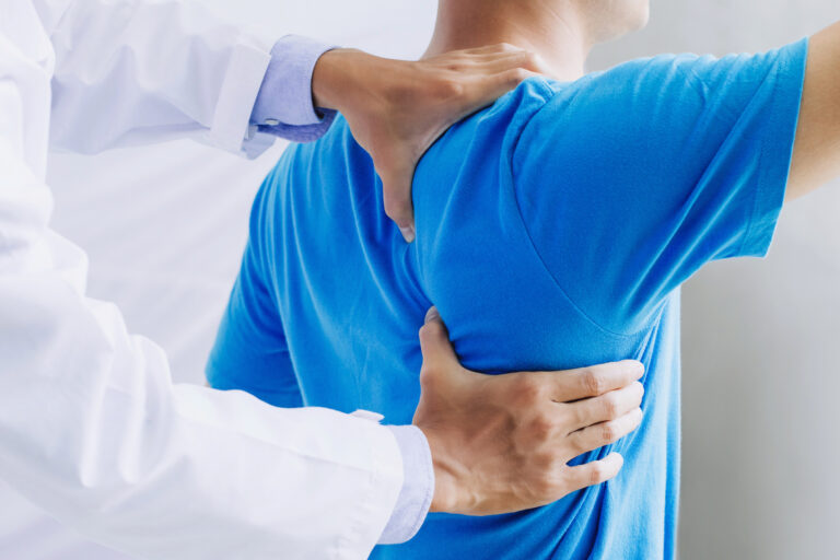 A chiropractor makes adjustments on a patient's back. The chiropractor focuses on the right shoulder blade area.